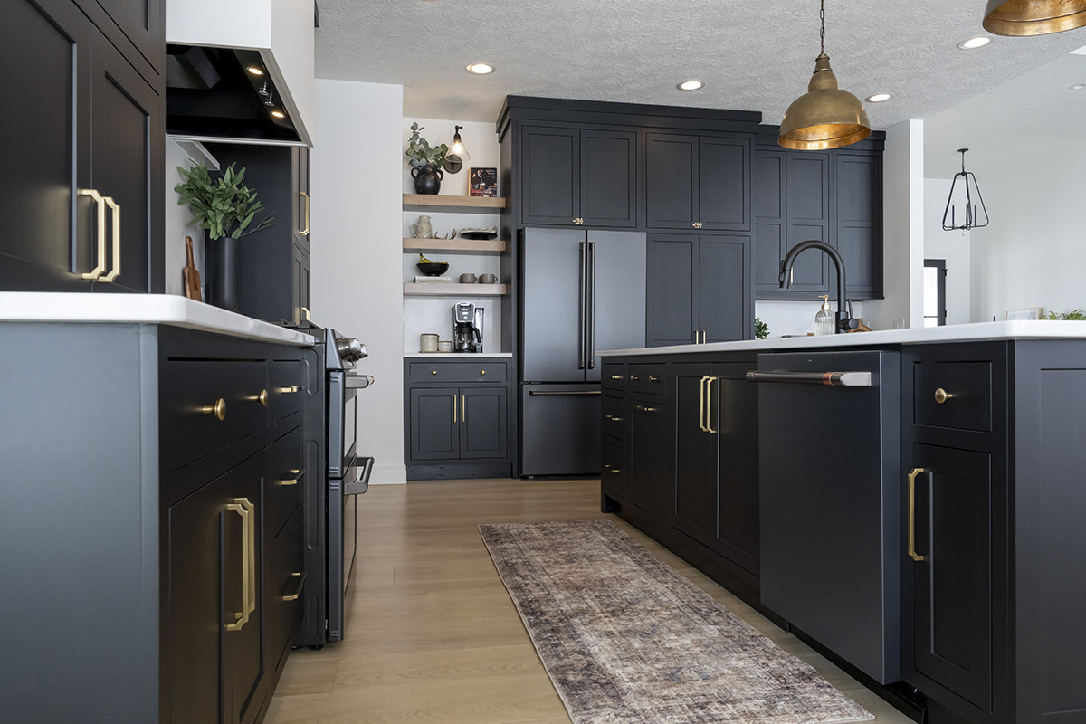 Black kitchen cabinetry with gold accents. Dark appliances such as a fridge and dishwasher accompany cabinetry.